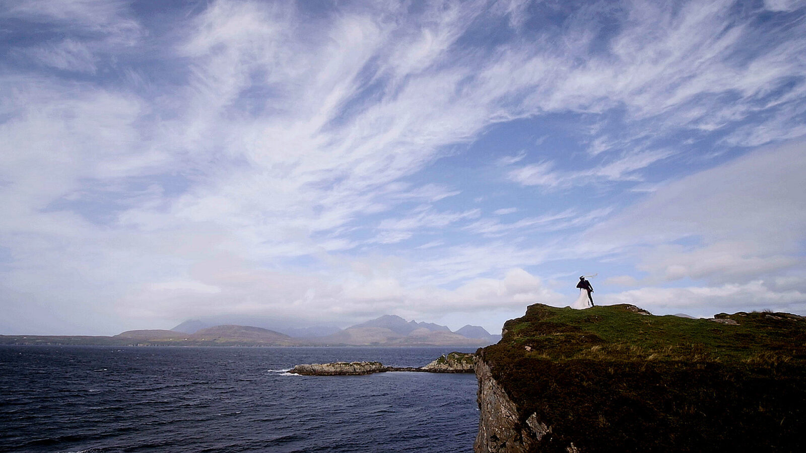 Aerial view of an elopement couple exploring the historic ruins and cliff edges of Dunscaith Castle on the Isle of Skye.