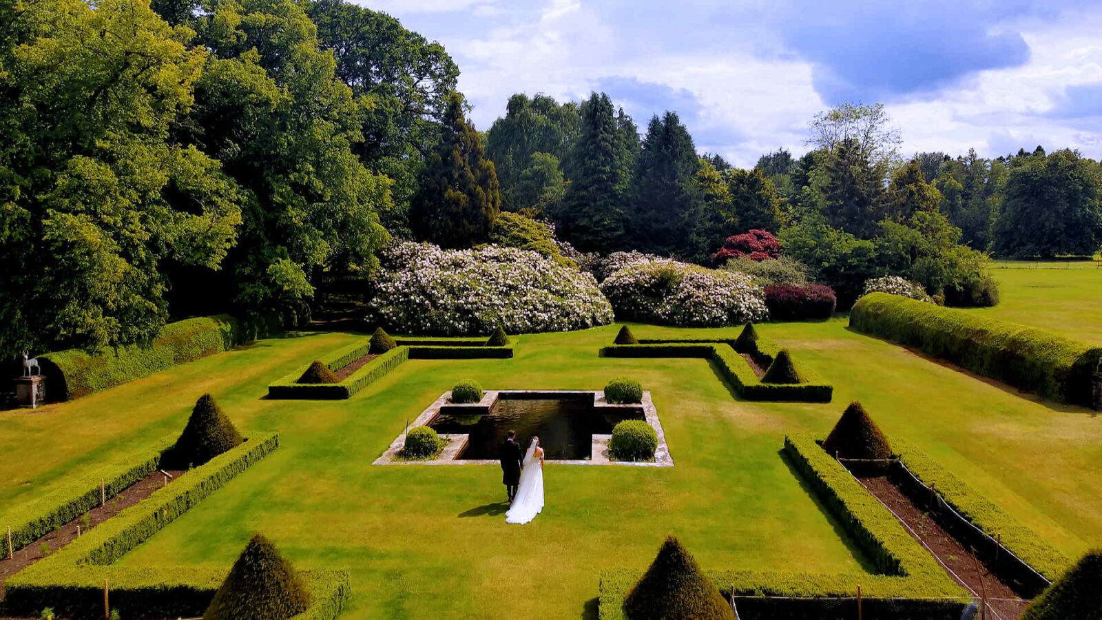 Aerial drone view of a bride and groom walking through the historic Walled Garden at Gordon Castle.